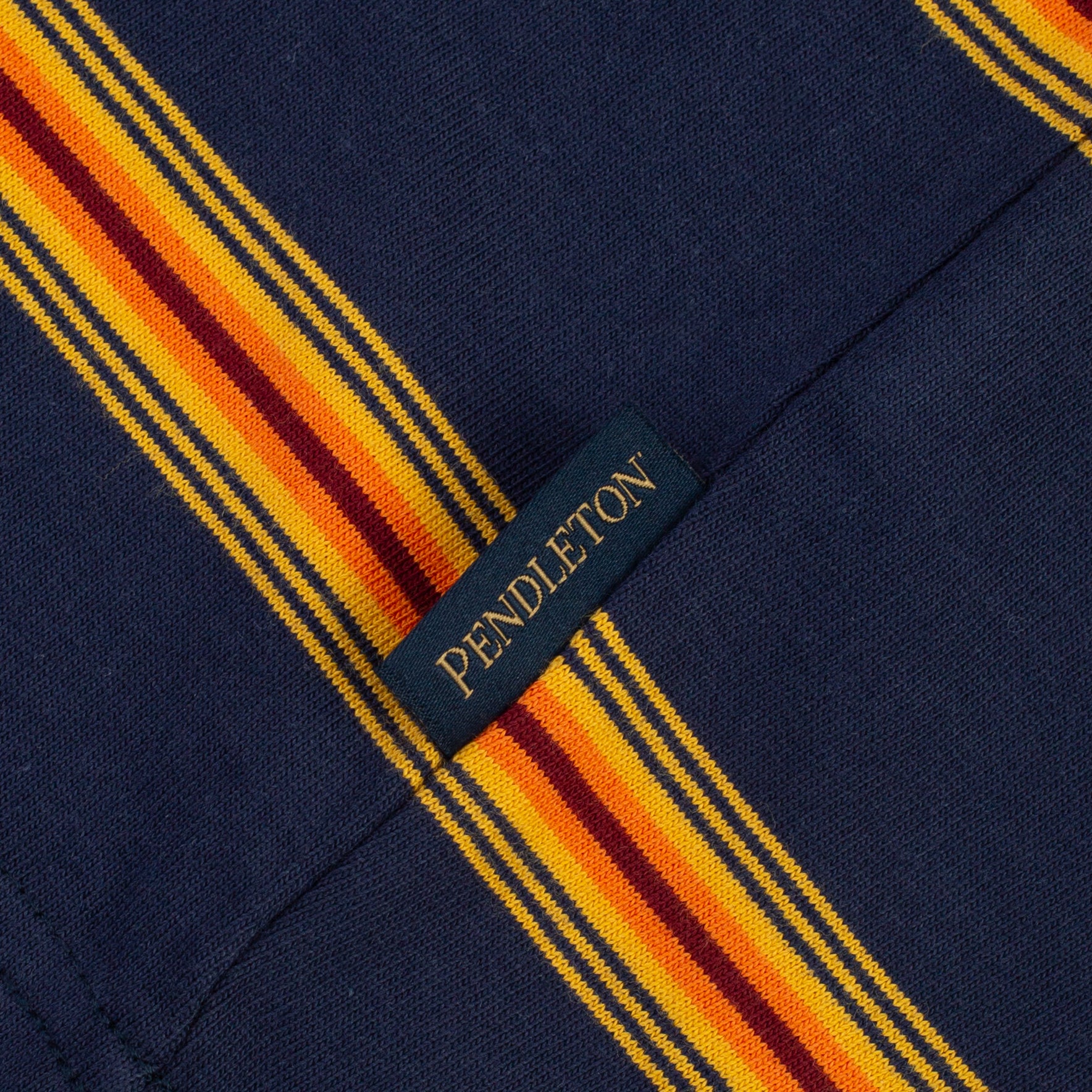 Close-up of a Pendleton fabric label sewn onto a navy blue garment with bold yellow, orange, and burgundy striped detailing.