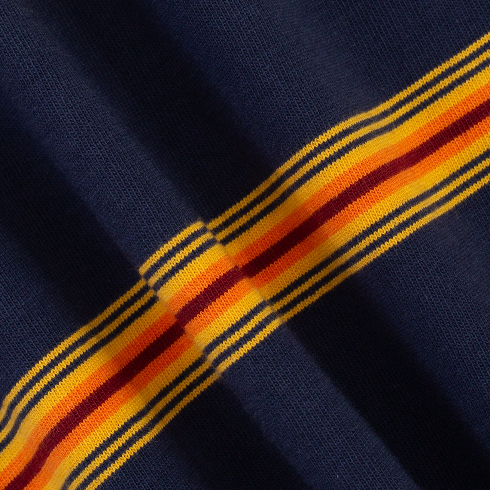 Close-up of a navy blue knit fabric with a diagonal striped pattern featuring yellow, orange, and red bands.