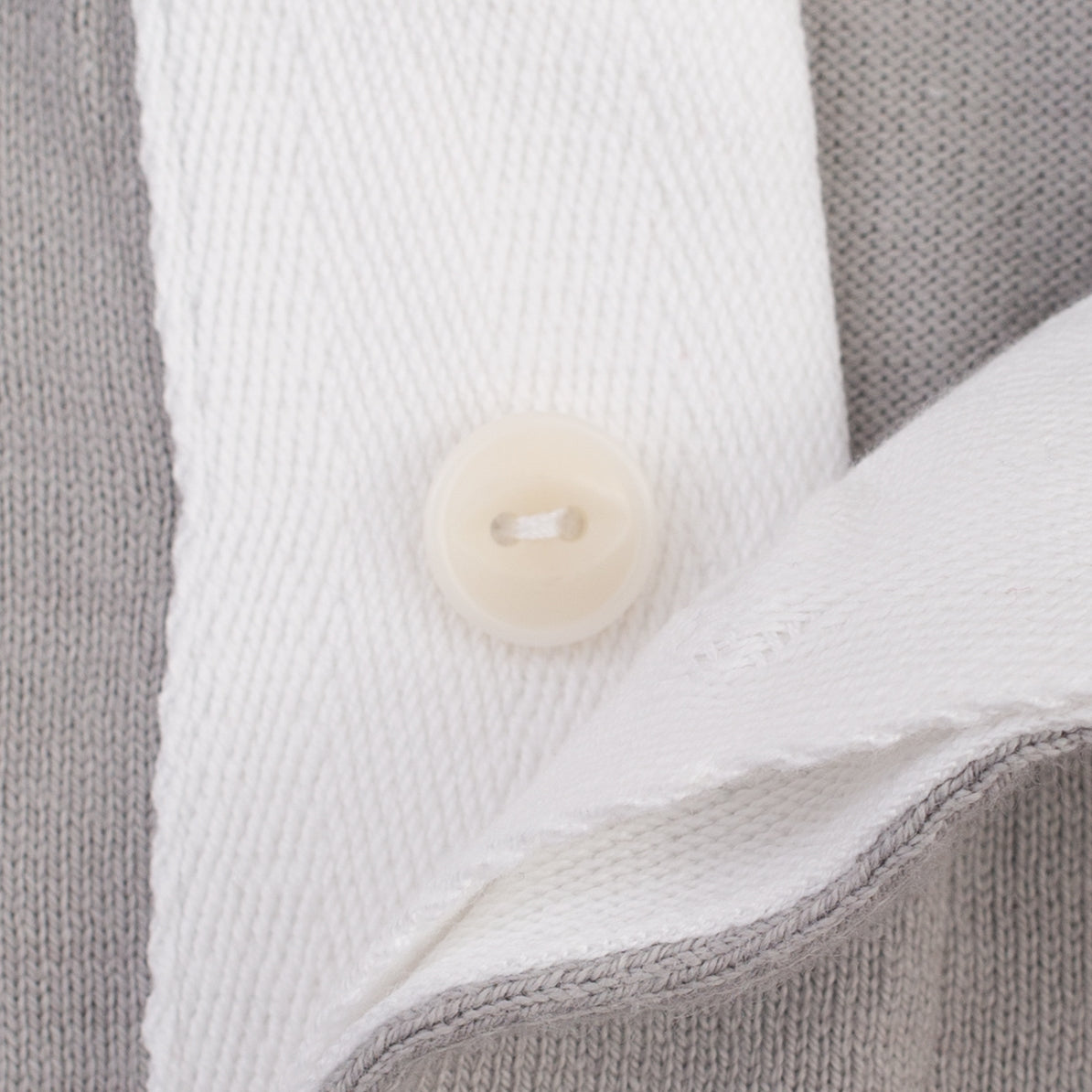 Close-up of a gray knit garment with a white collar and a round off-white button.
