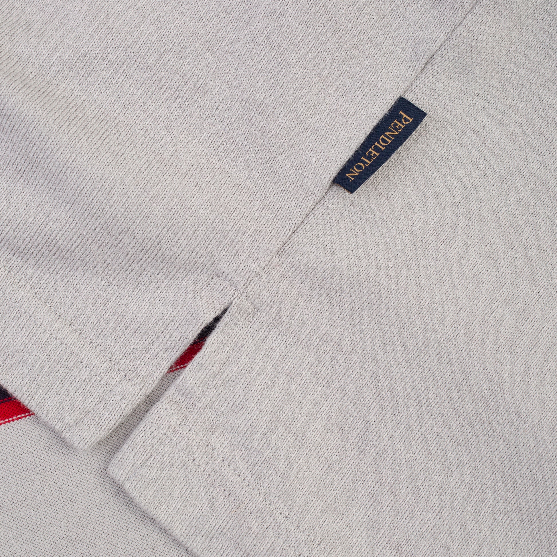 Close-up of a light gray woven fabric garment with a small navy brand tag reading PONDUTTON in gold lettering.
