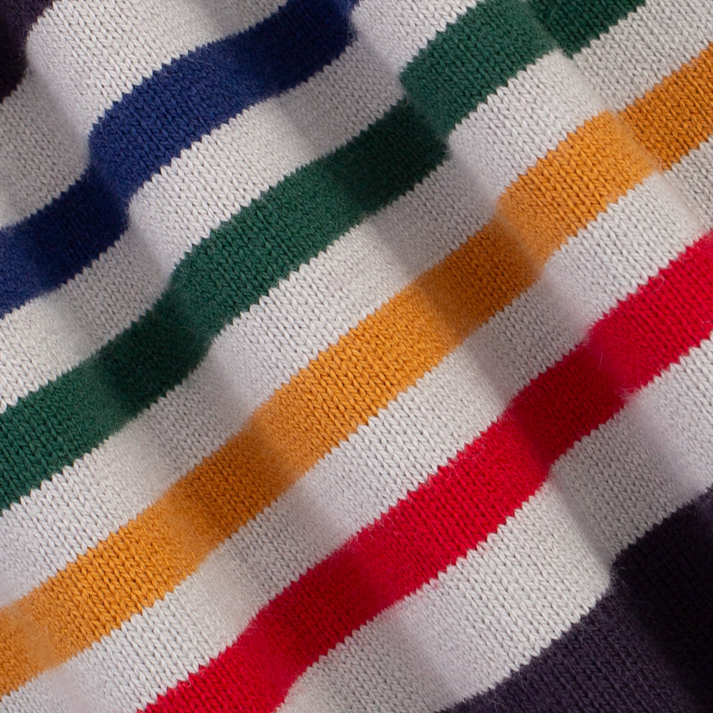Close-up of a knitted fabric with diagonal stripes in white, green, navy, orange, and red.