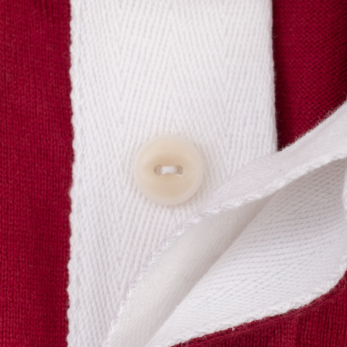 Close-up of a knit garment showing a white collar with a cream-colored button, bordered by deep red fabric.