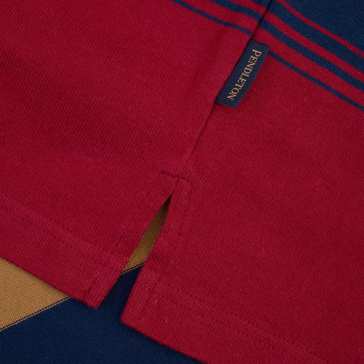 Close-up of a red knit garment with navy blue stripes near the collar and a small navy brand tab reading Pendleton.