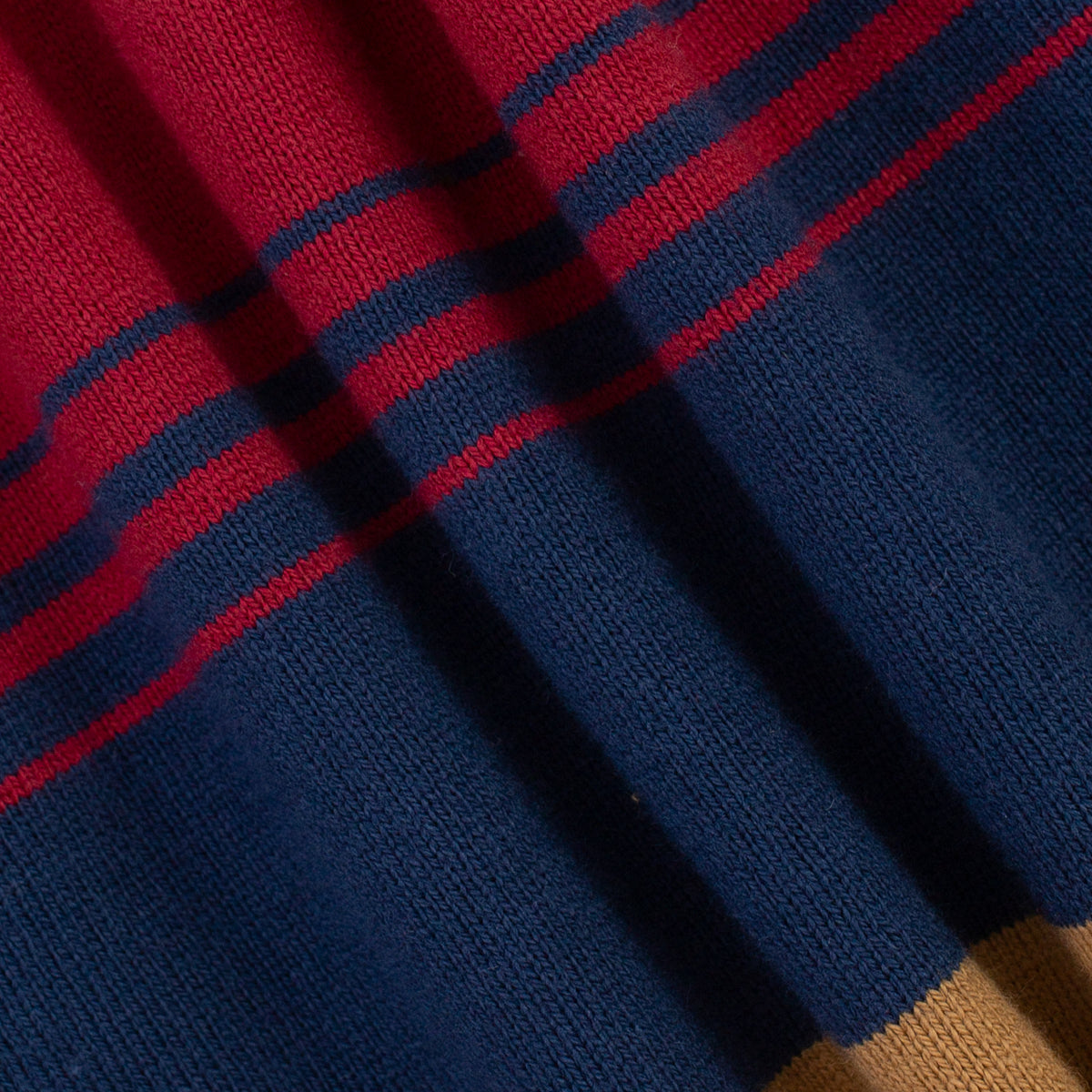 Close-up of a knitted fabric with diagonal stripes in navy blue, red, and a small tan section at the bottom right.